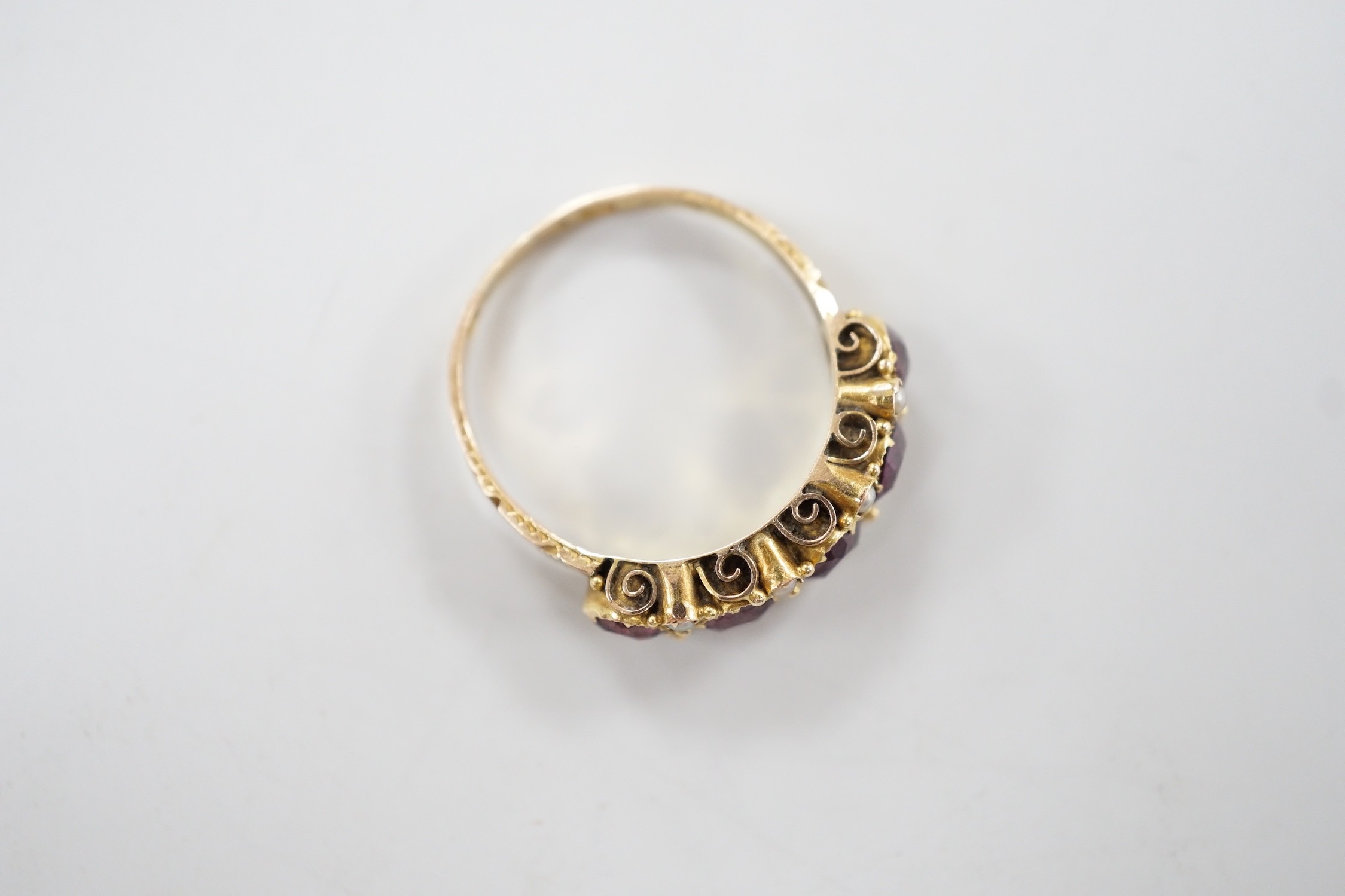 A late Victorian 15ct gold and graduated five stone garnet set half hoop ring, with split pearl spacers, size, P/Q, gross weight 2.5 grams.